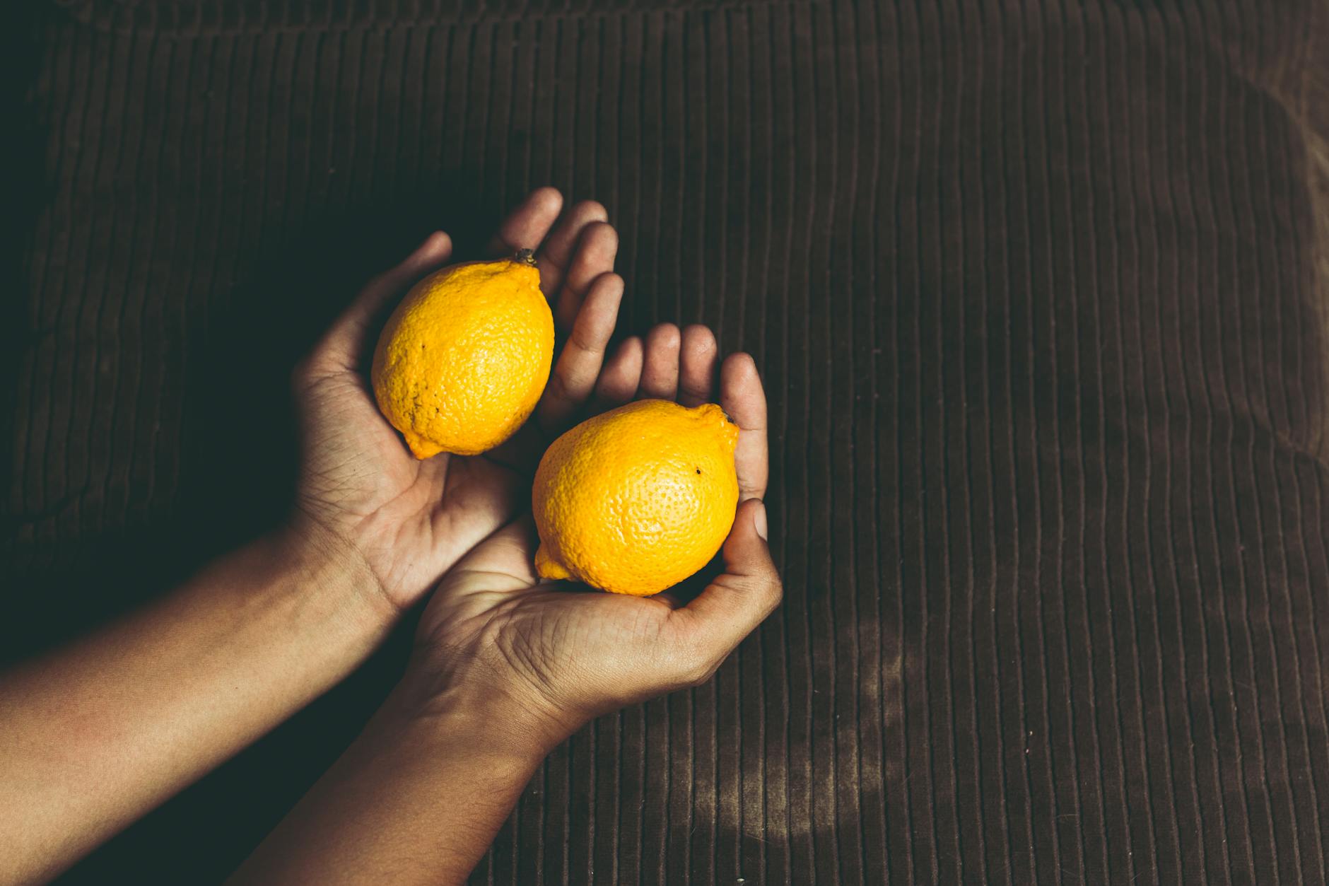 Due limoni freschi tenuti in mani a coppa su una superficie marrone