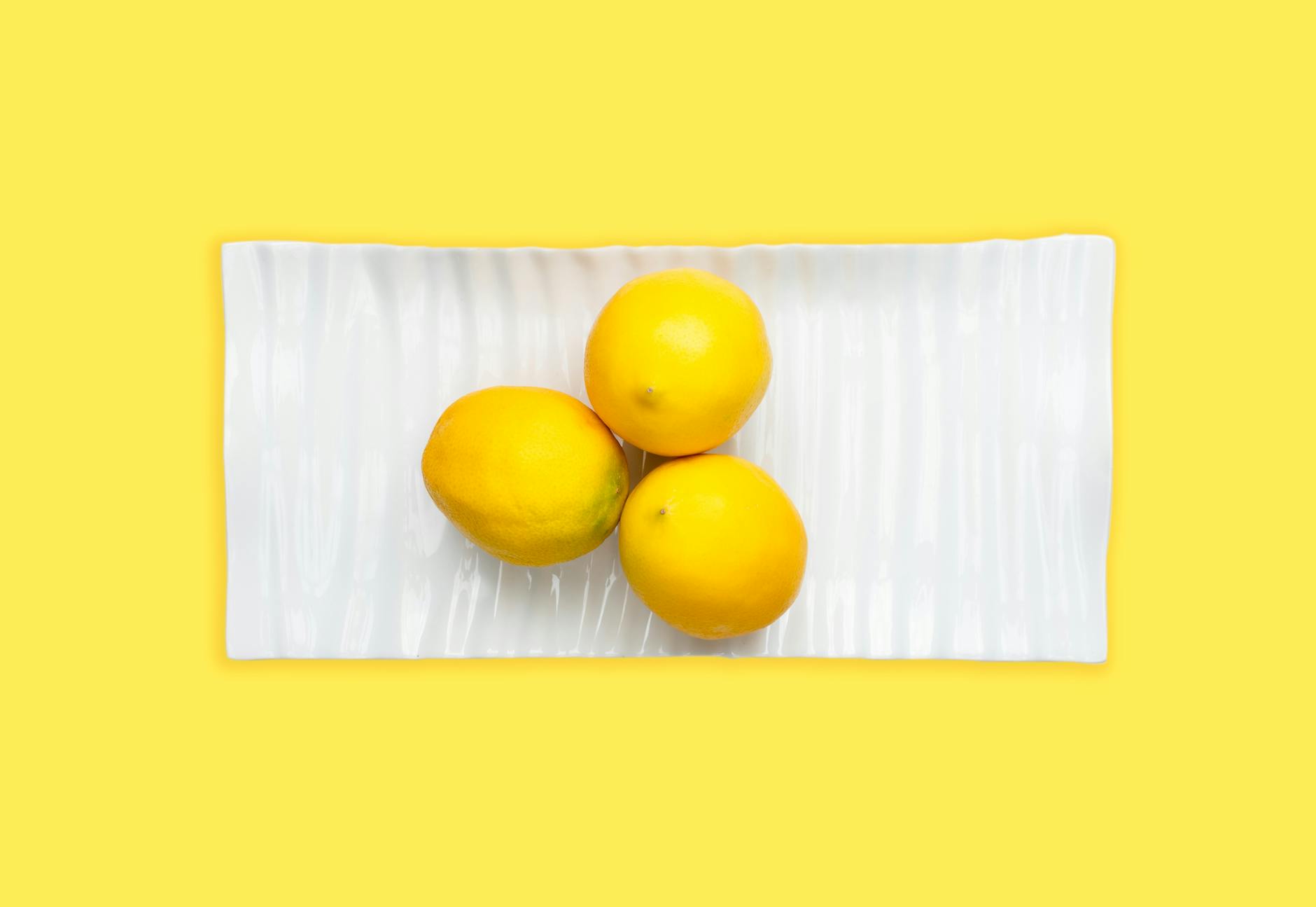 Close-up of vibrant lemons arranged on a white plate with a yellow background