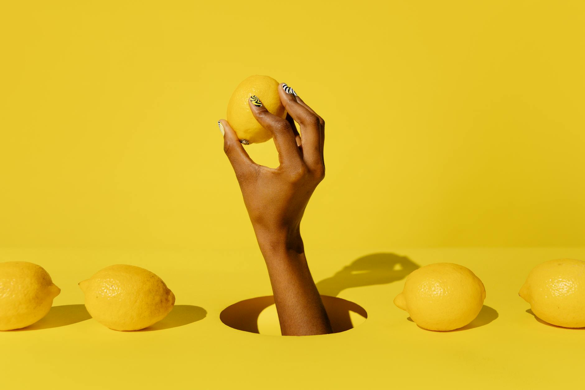 Hand holding a fresh lemon against a vivid yellow background, symbolizing renewal and fresh pleasure