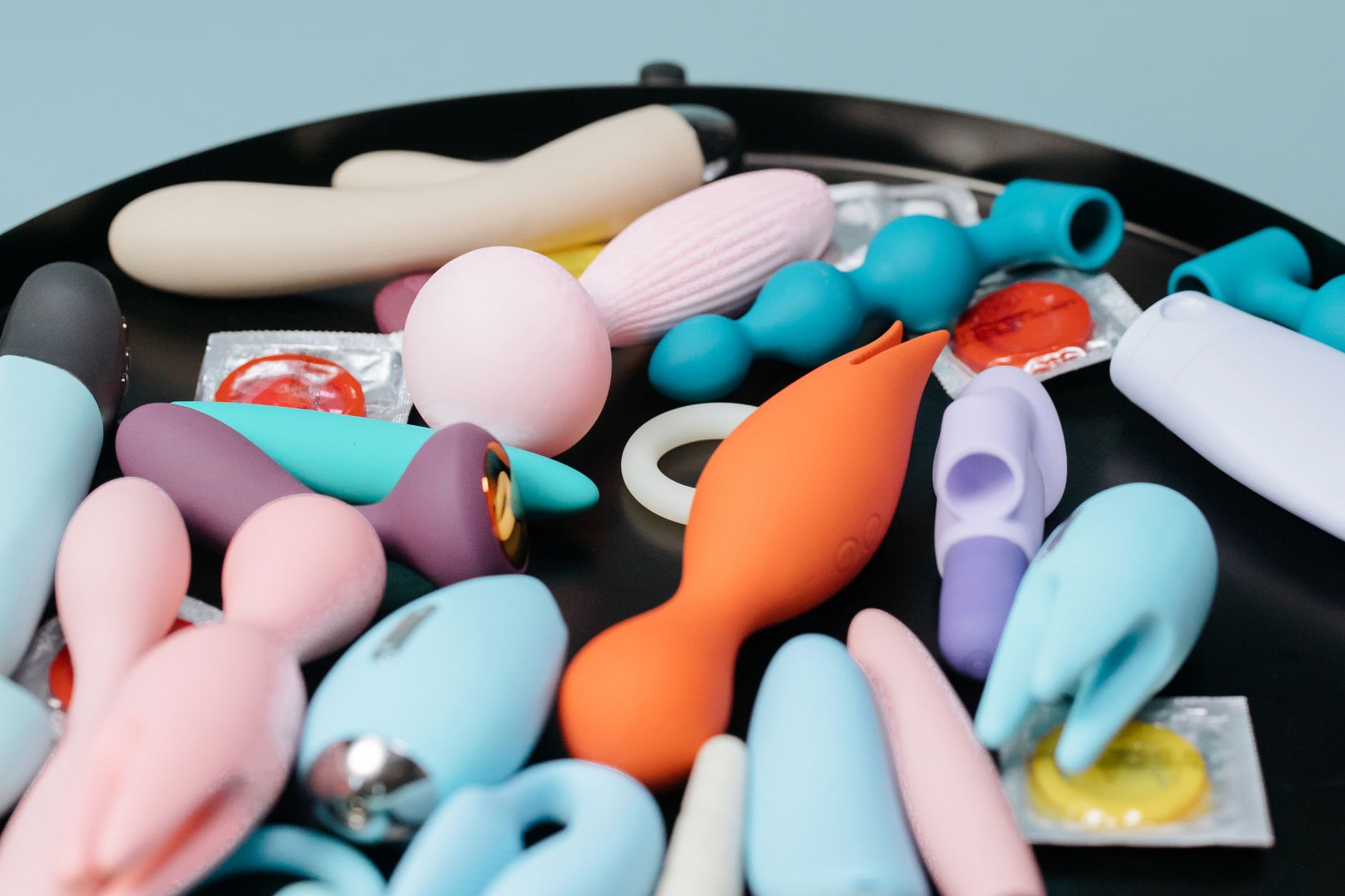 Woman holding blue and pink silicone vibrators in a thoughtful moment