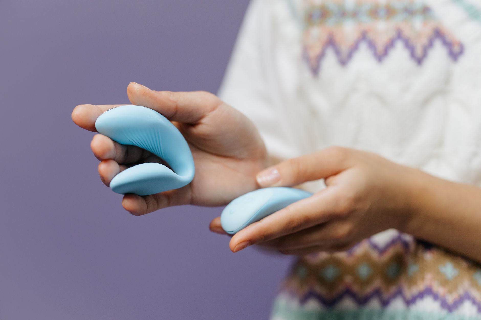 Intimate close-up of hands holding a sleek blue vibrator against a purple background.
