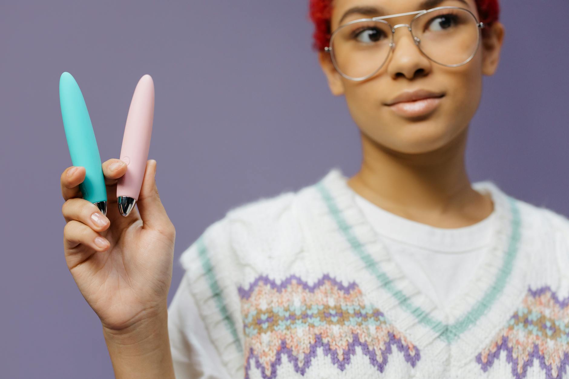 A woman holds colorful vibrators against a purple background, representing the reintroduction of pleasure tools
