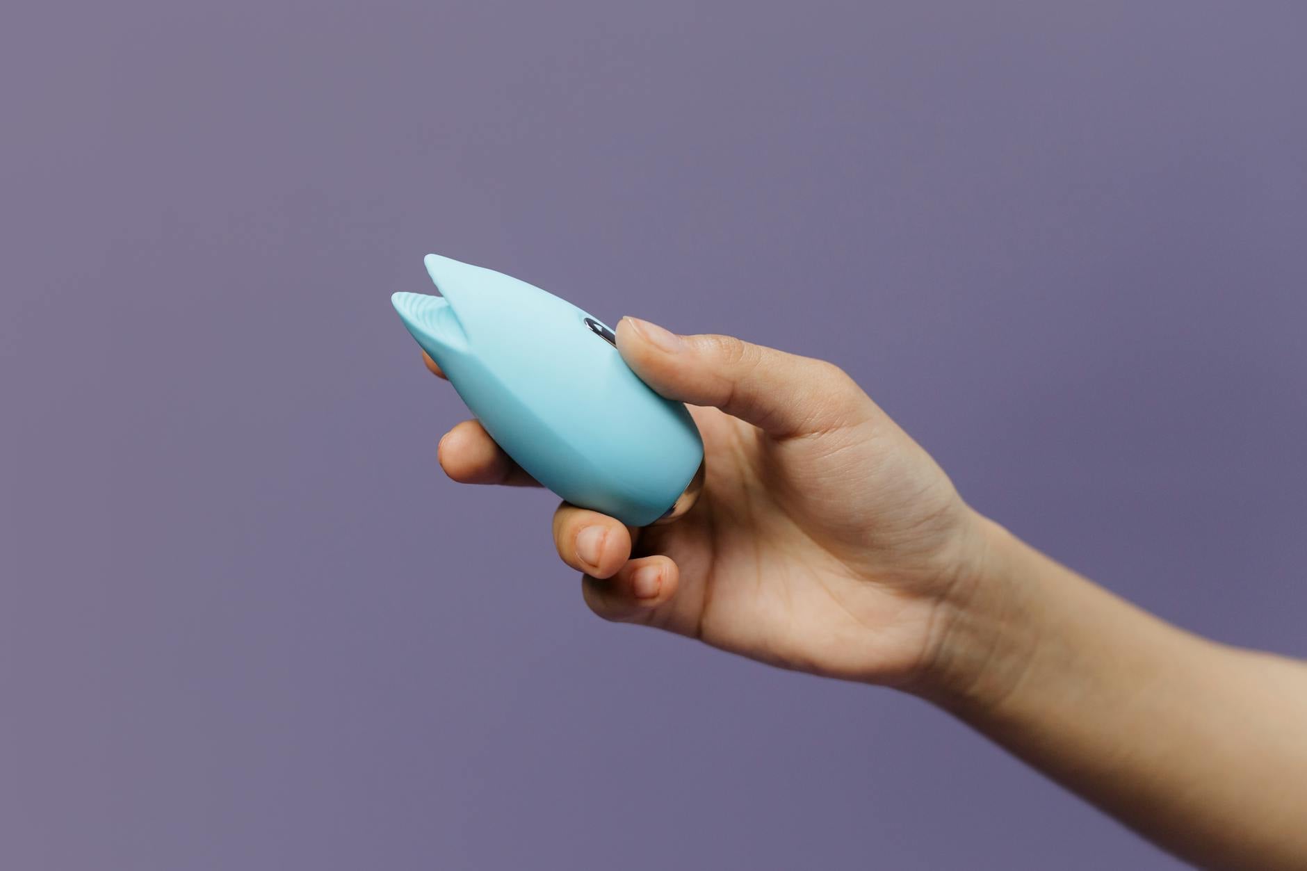 A blue lemon clitoral vibrator held in hand against a purple background